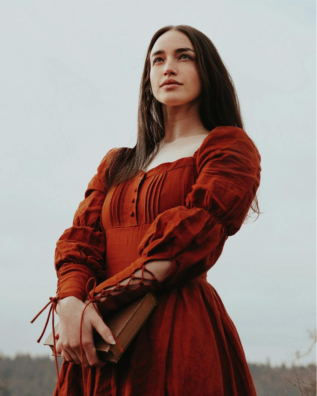 model in a medieval red dress with laced cuffs holding a book
